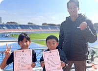 競技場で賞状を持つ子どもとコーチ(大会への出場)